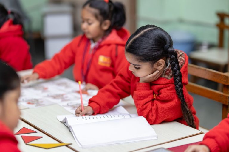 Student cu caiet deschis la o masă din bibliotecă, în lumina de după-amiază